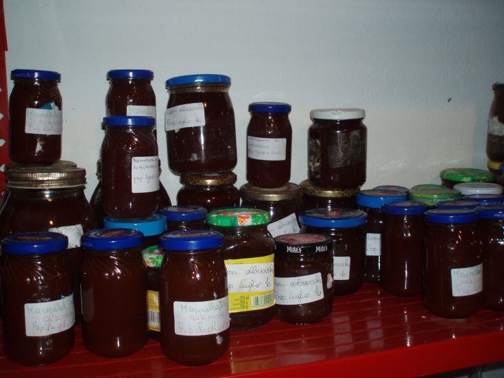 Diverse bottiglie di marmellata disposte su uno scaffale in un contesto semplice e rustico.