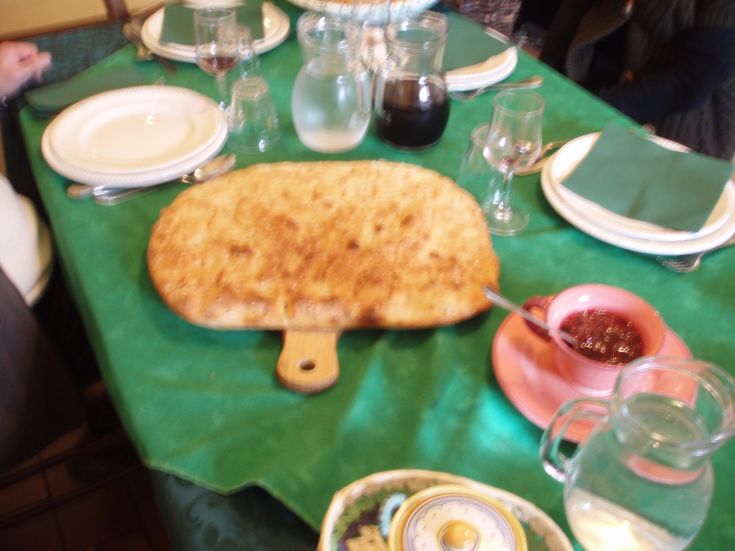 Su una tavola rustica, una focaccia dorata è pronta per essere gustata, affiancata da un vasetto di marmellata.