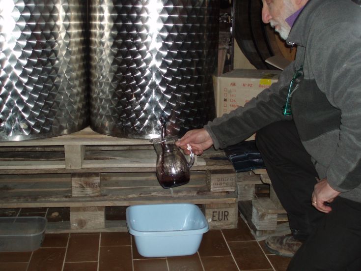 Un uomo versa vino da una caraffa in un recipiente blu, in un contesto di lavorazione del vino.