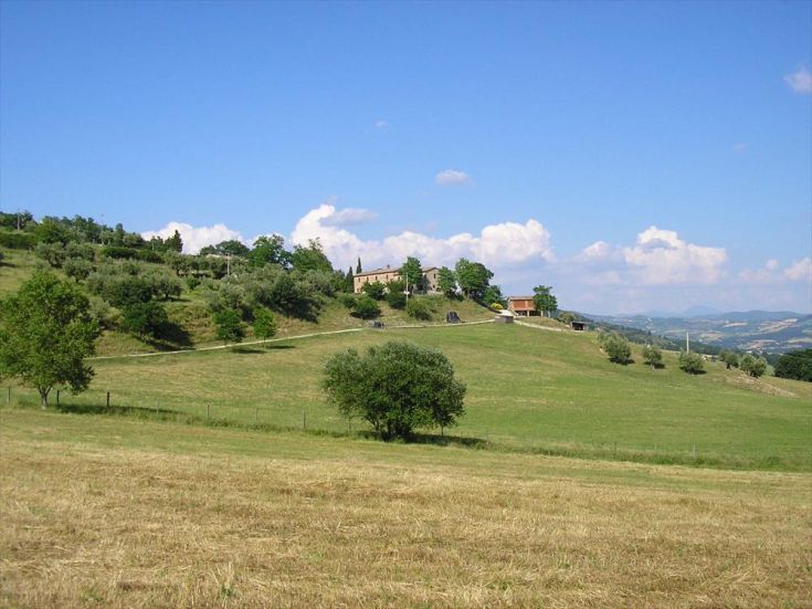 Serene Umbrian countryside scene with rustic houses, green spaces, and a clear sky.