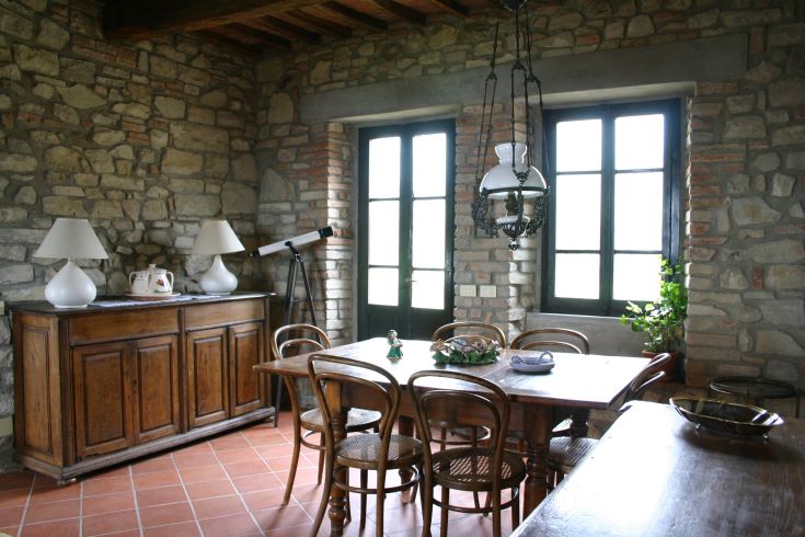 The image shows a living room with stone walls and wooden furniture. Windows let in natural light.