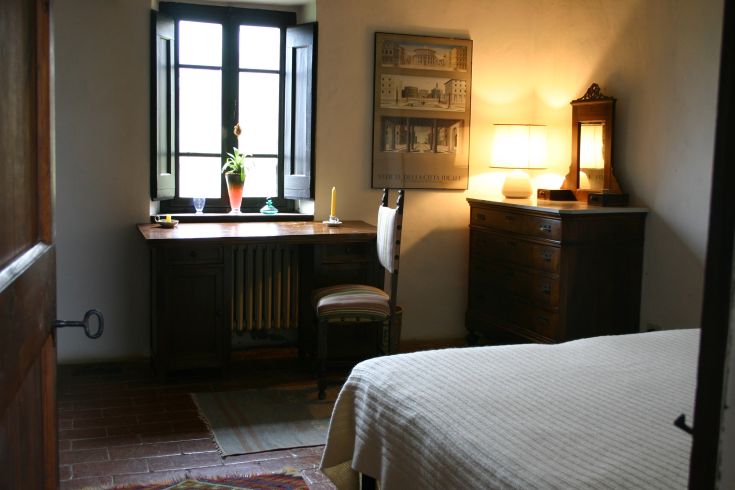 A simple room with a desk and soft lighting, featuring windows that illuminate the space. Wooden furniture.
