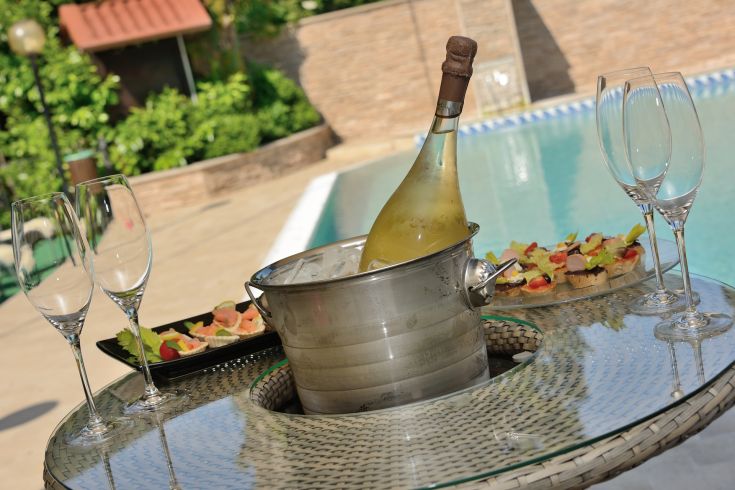 Une table près d'une piscine avec du champagne et des collations légères, idéale pour un moment de détente en extérieur.