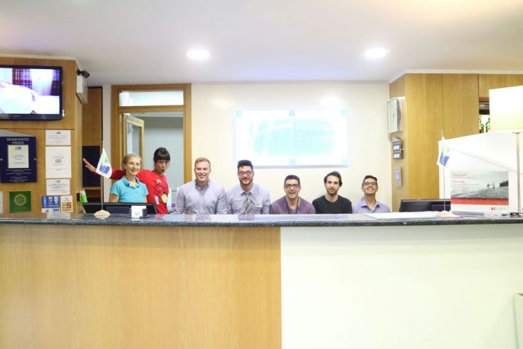Several smiling people are at the reception of a building, ready to welcome guests.