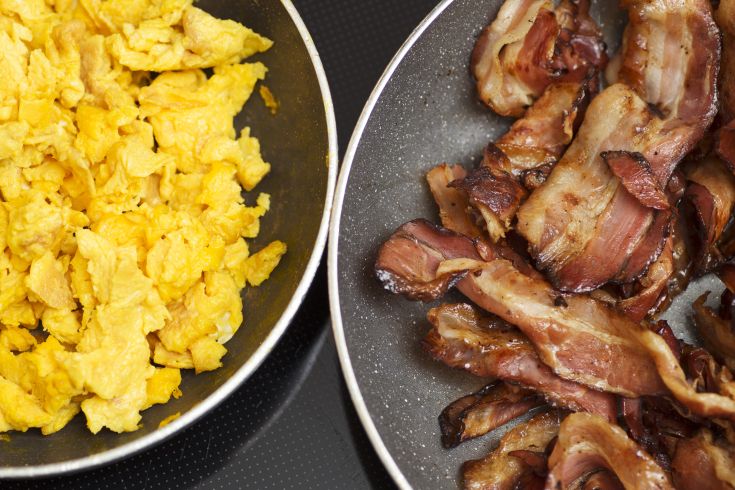 Scrambled eggs served with crispy bacon in a frying pan.