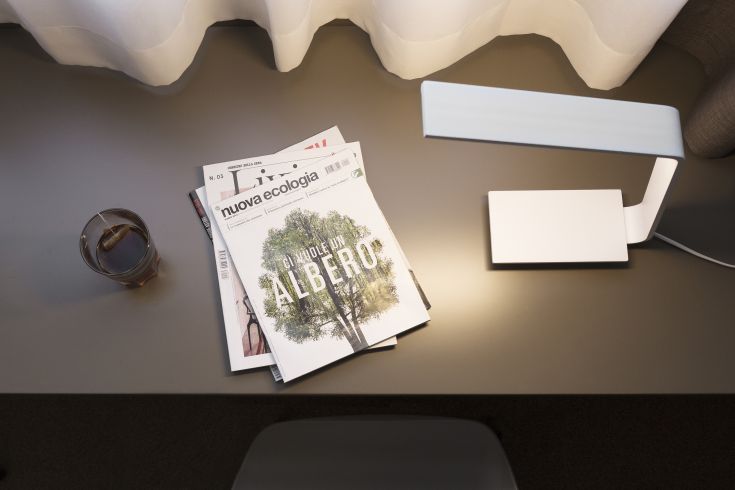 On a modern table, there is a stylish lamp, magazines, and a glass with a beverage.