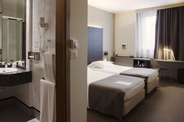 Simple and well-organized hotel room with single beds, a bathroom with amenities, and a desk.