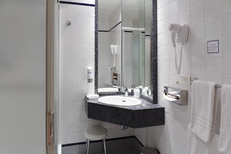 Practical and well-furnished hotel bathroom with sink, mirror, towels, and hairdryer available.