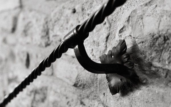 Detail eines Metallhalters, der an einer Natursteinwand montiert ist.