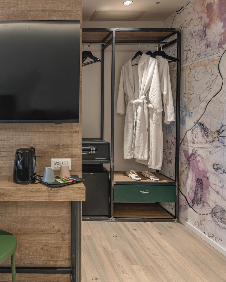 Innenansicht eines Hotelzimmers mit einem offenen Kleiderschrank und weißen Bademänteln. Der Wohnbereich ist einfach und gemütlich.