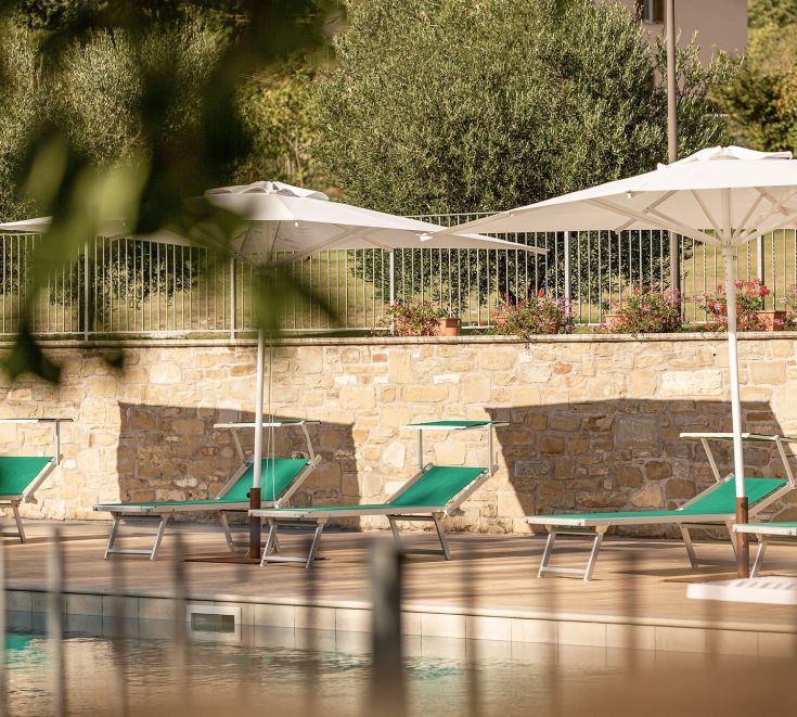 Poolbereich mit Sonnenschirmen und Liegen, umgeben von dem Grün eines gut gepflegten Gartens.