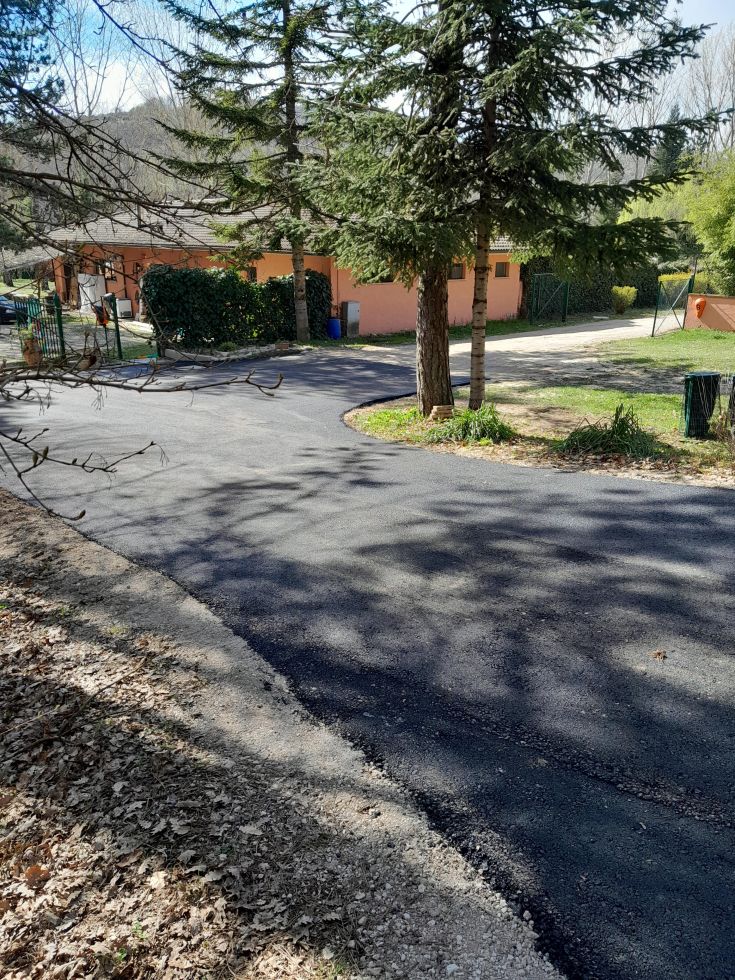 A stone road stretches between trees, with a small rustic building visible in the background.