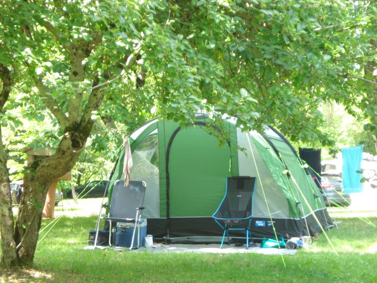 Green camping tent set in a serene green area surrounded by trees, perfect for a peaceful camping experience.