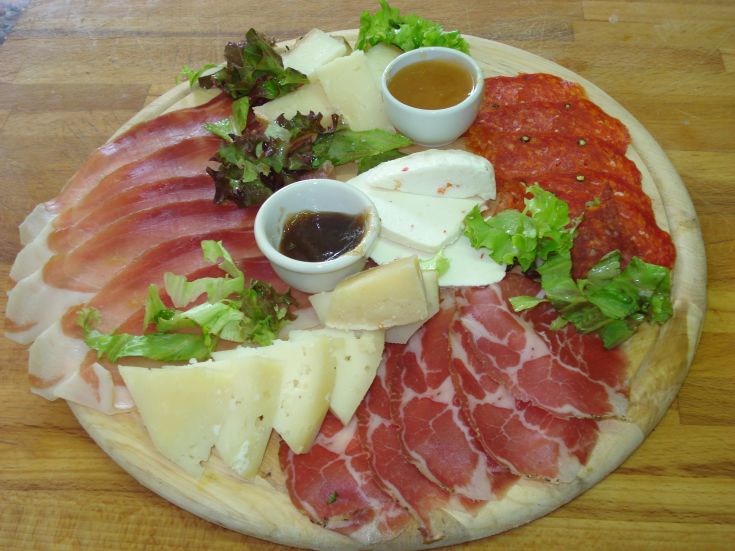 A mixed platter of cured meats and cheeses, served with a selection of sauces and a side of fresh salad.