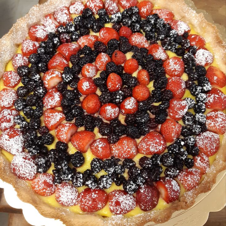 Fruit tart with a shortcrust pastry base, filled with cream and topped with fresh strawberries and blackberries, dusted with icing sugar.