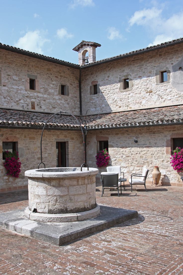 Une cour tranquille avec un puits, dotée de sièges et de plantes, qui reflète une ambiance historique.