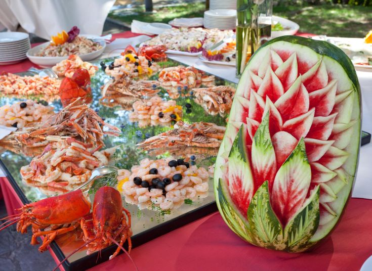 Un buffet de fruits de mer disposé en plusieurs plats, décoré de garnitures de pastèque. Un mélange de couleurs et de saveurs.
