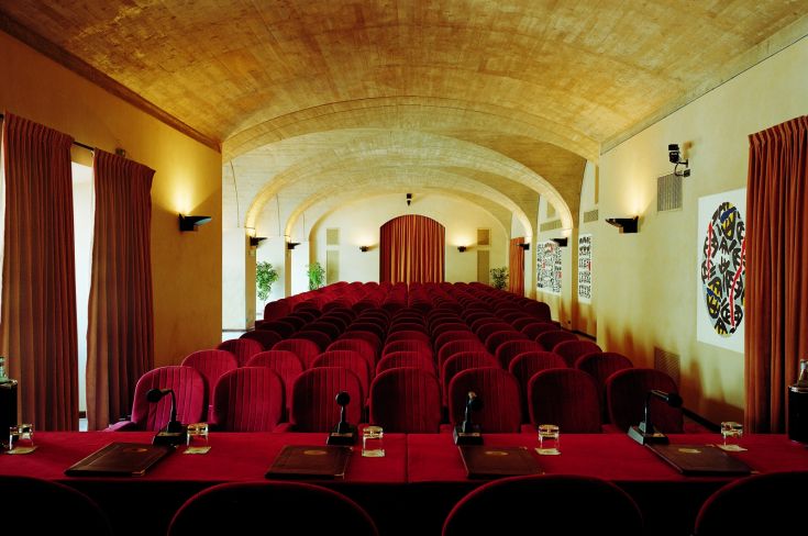 Une salle de l'Hôtel Park aux Cappuccini avec des chaises rouges, située dans un ancien monastère, avec des arches et des détails modernes.