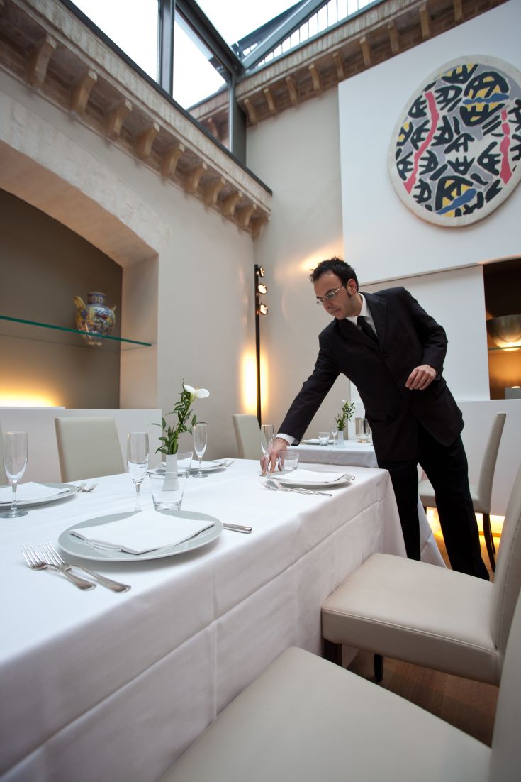 Un serveur préparant soigneusement une table dans un restaurant moderne, avec des détails simples et soignés.