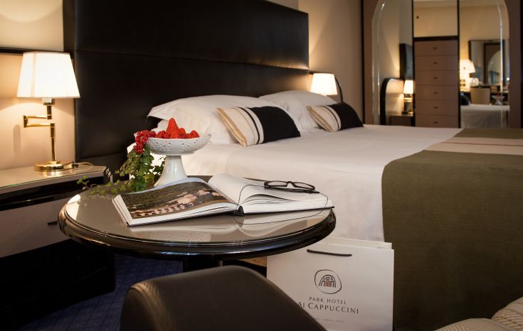 Chambre d'hôtel simple avec un lit double, des livres sur une table de nuit et un plateau de fruits frais.