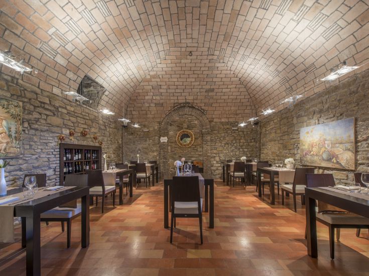 Innenansicht eines gehobenen Restaurants mit Steinwänden und einem Gewölbe, mit für Gäste gedeckten Tischen.