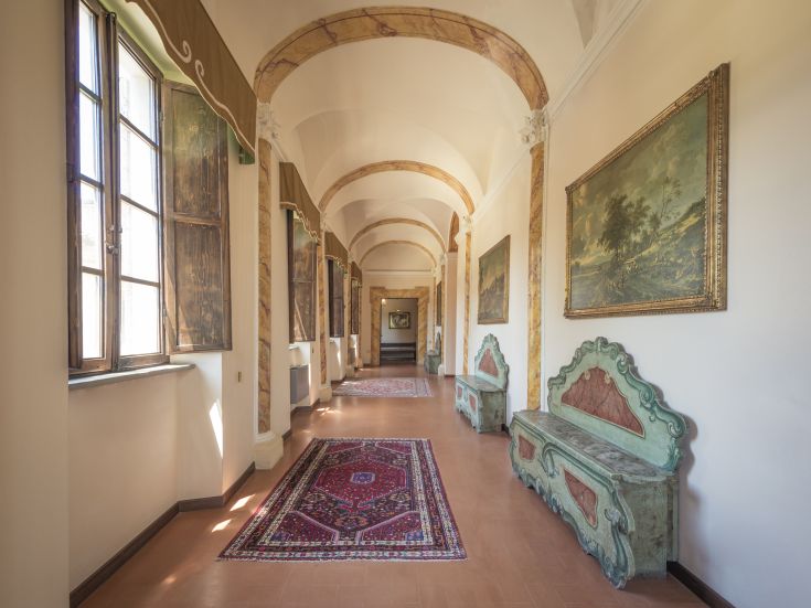 Ein Flur in einer historischen Villa, ausgestattet mit antiken Möbeln und gut beleuchtet von großen Fenstern.