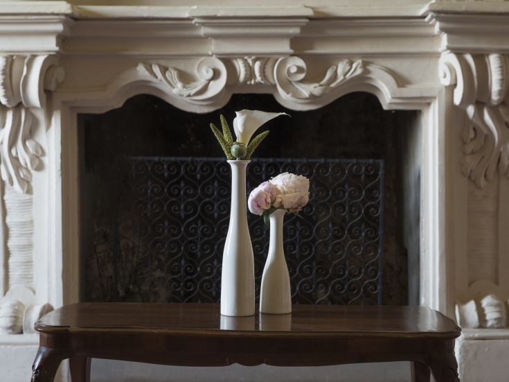 Einfache Blumenarrangement mit weißen Vasen auf einem Holztisch. Im Hintergrund ist ein dekorierter Kamin zu sehen.