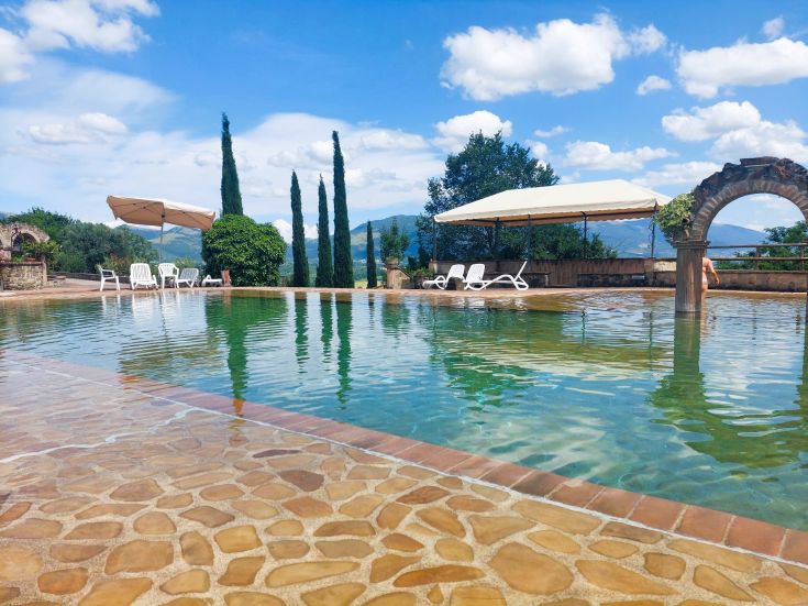 Schwimmbad in einer natürlichen Umgebung, umgeben von grünen Hügeln.