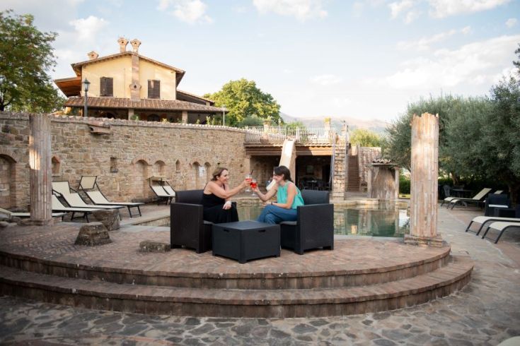 Zwei Frauen stoßen am Rand eines Pools in der entspannenden Atmosphäre eines Gartens an.