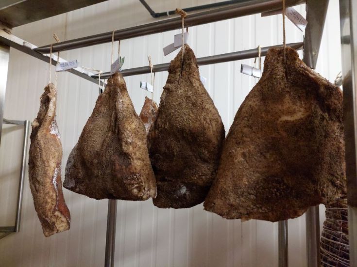 Ein rustikaler Arbeitsbereich mit hängenden luftgetrockneten Schinken, bereit zum Verkauf.