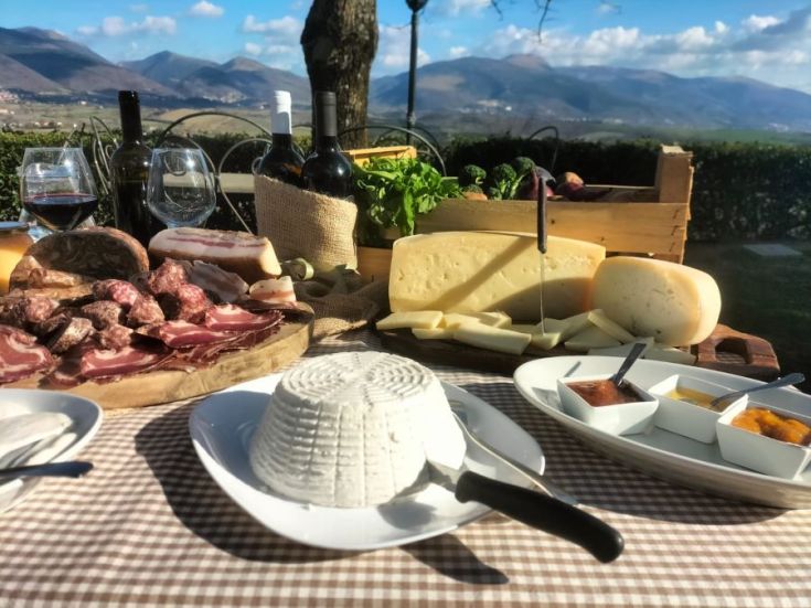 Eine Auswahl an Wurstwaren und Käsesorten auf einem Tisch, mit sanften grünen Hügeln im Hintergrund.