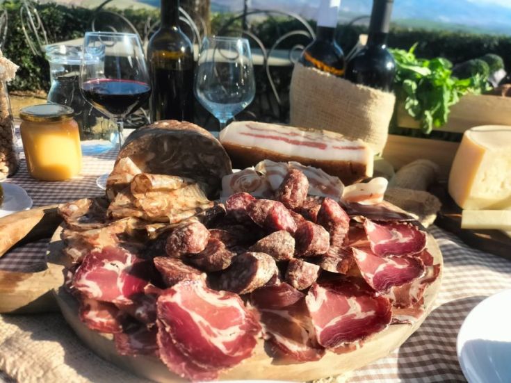 Ein Plattenangebot mit Wurstwaren, serviert mit traditionellen Gerichten und Weinen in einer natürlichen Umgebung.