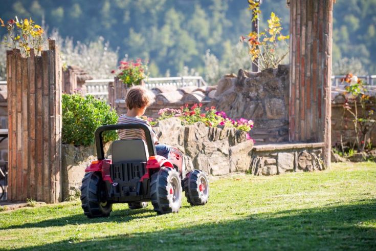 Ein Kind spielt mit einem Spielzeugtraktor in einem gepflegten, weitläufigen Garten.