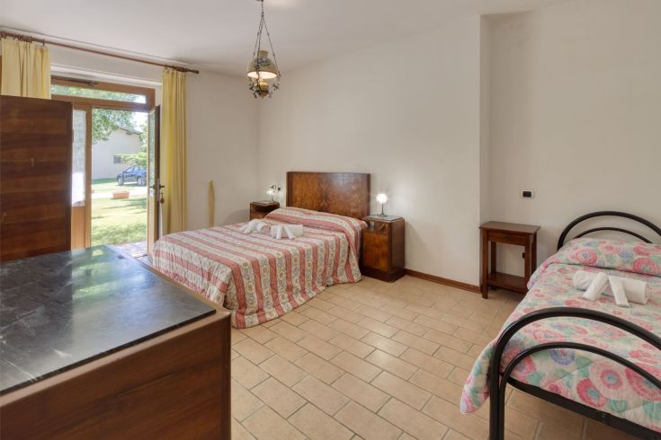 Camera in agriturismo con letti matrimoniali e singoli, ben illuminata e circondata dalla vegetazione.