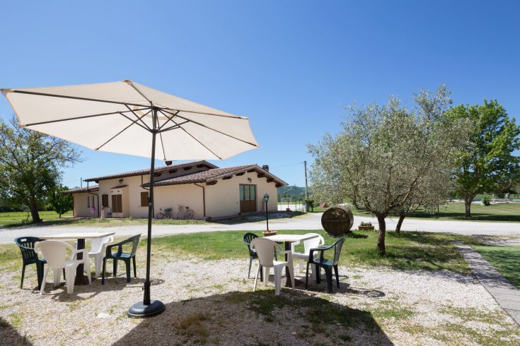 Spazio all'aperto con tavoli e ombrelloni, circondato da piante e situato accanto a un edificio.