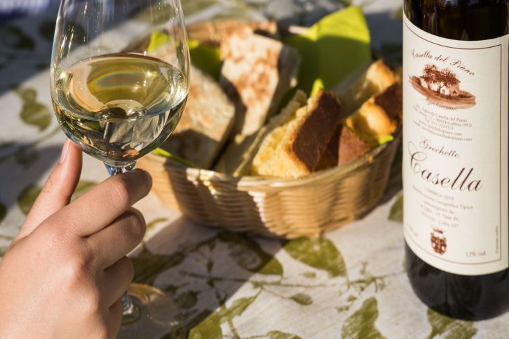 Un calice di vino bianco accanto a un cestino di pane fresco, in un contesto elegante e rilassato.