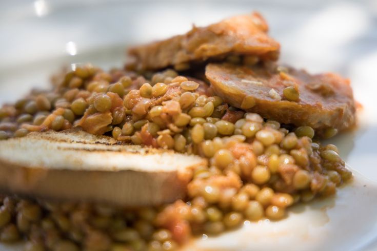 Piatto di lenticchie con carne e fette di pane croccante, adatto per un pasto ricco e sostanzioso.