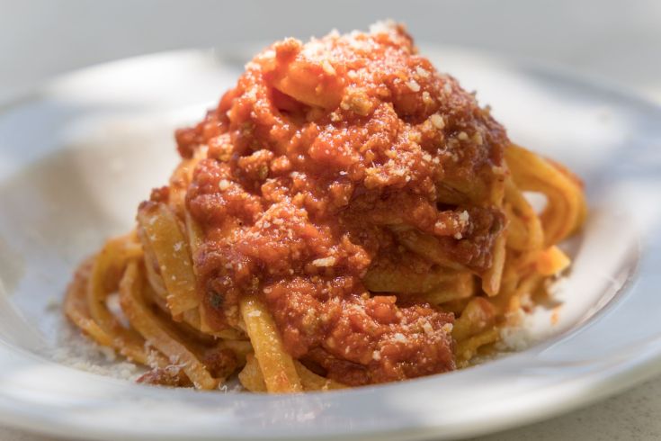 Un piatto di pasta con sugo rosso, servito caldo e guarnito con formaggio grattugiato.