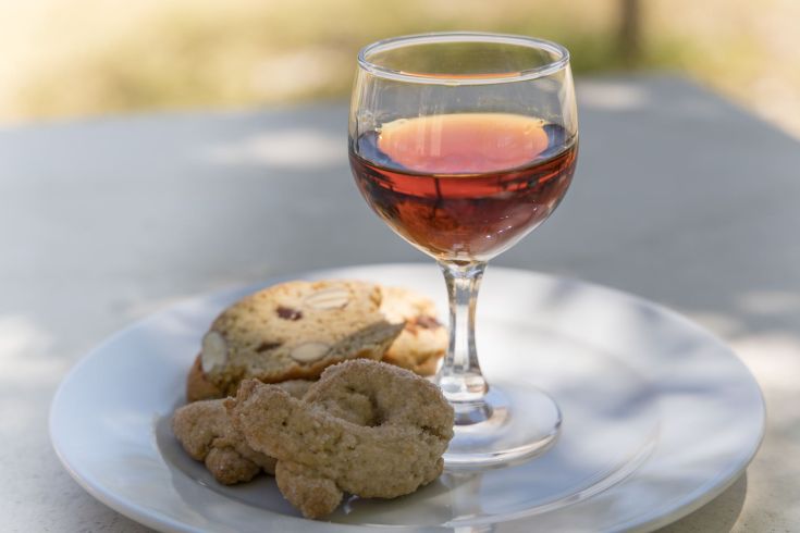 Un bicchiere di vino rosso accompagnato da biscotti su un piatto bianco, inseriti in un contesto naturale.