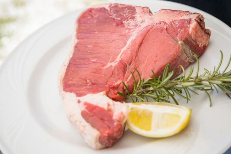 Bistecca cruda con fette di limone e rametto di rosmarino, pronta per la cottura.