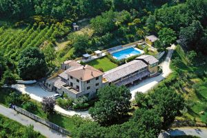 Scena aerea di un edificio rurale circondato da vegetazione, con una piscina visibile nelle vicinanze.