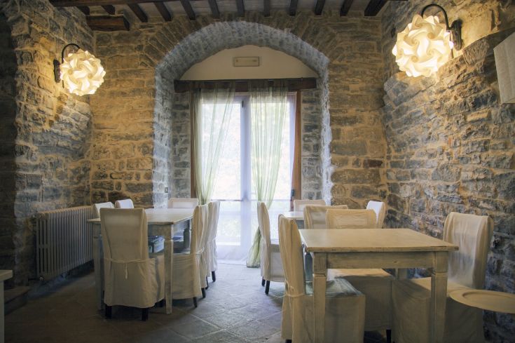 Interno di un ristorante con tavoli e sedie bianche, illuminati da lampade dal design contemporaneo.