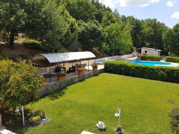 Un giardino ben mantenuto con una piscina circondata da alberi e una veranda tranquilla.