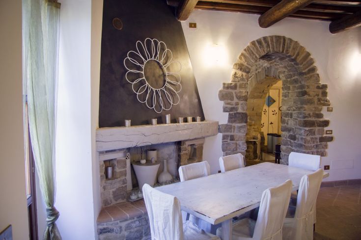 Interno confortevole con un tavolo, un camino e archi in pietra che creano una calda atmosfera.