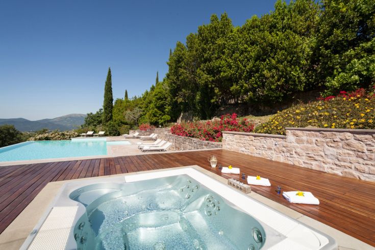 Jacuzzi in un ambiente curato con giardini fioriti e una piscina che offre un panorama rilassante.