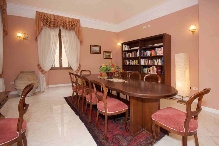 Ambiente di una sala con tavolo centrale e una libreria, adatto per incontri e momenti di svago.