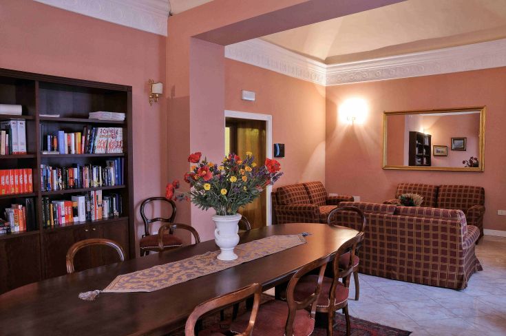 Stanza luminosa con un grande tavolo decorato con fiori, librerie e divani disposti in modo confortevole.