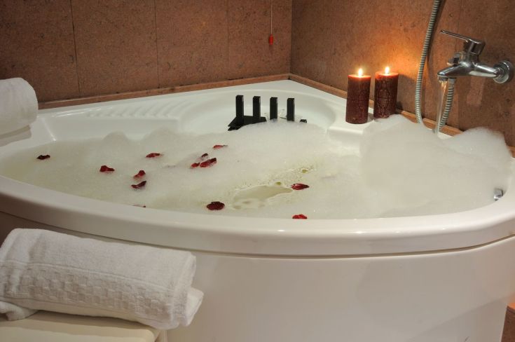 Vasca da bagno con schiuma e petali di rose, candele accese creano un'atmosfera piacevole per rilassarsi.