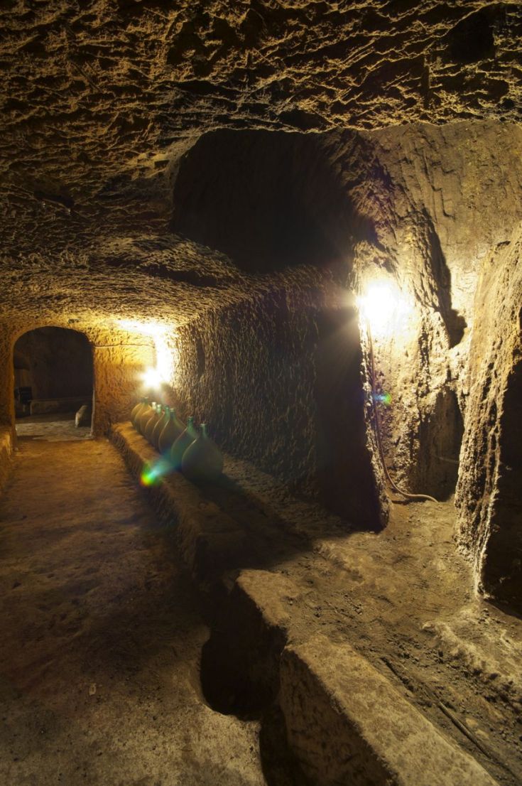 Una cantina storica con luci soffuse che mettono in risalto le pareti di pietra e una serie di anfore disposte.