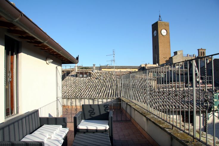 Terrazza che si affaccia sui tetti della città, con alcune poltrone e un campanile in lontananza.